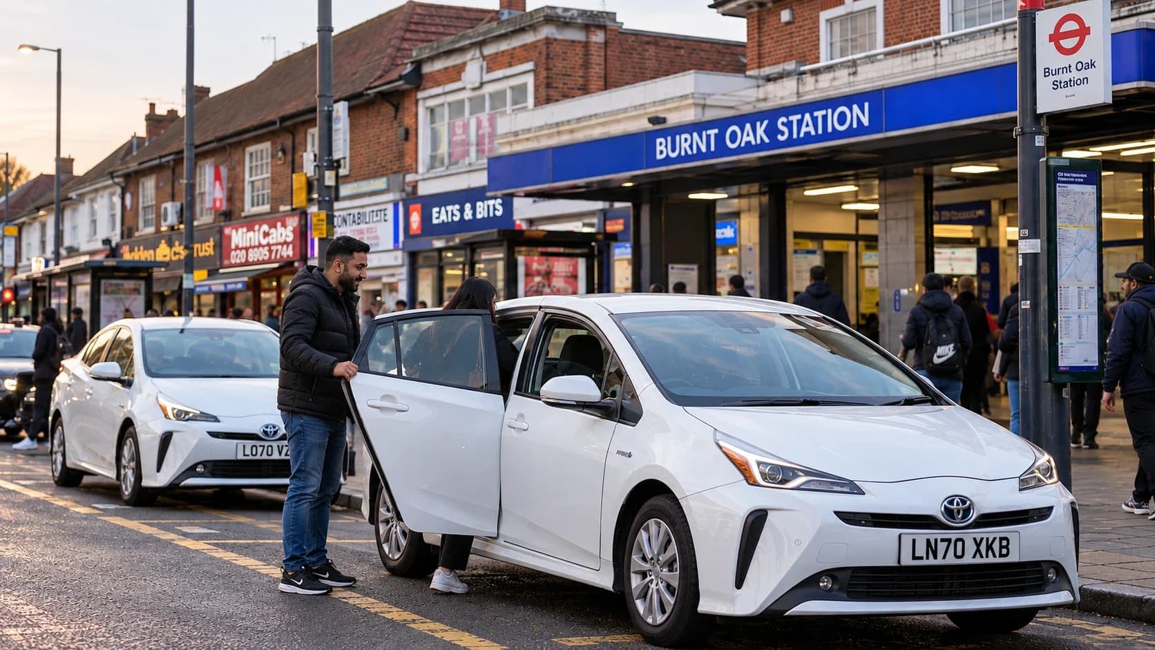 A Watling Cars driver opening the door for a passenger outside Burnt Oak station